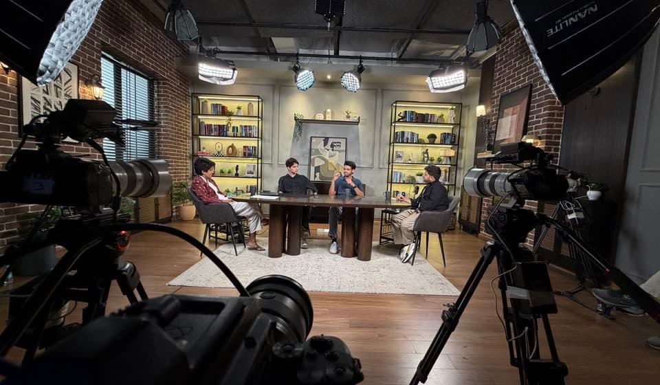 A four-person podcast shoot seen from behind the cameras